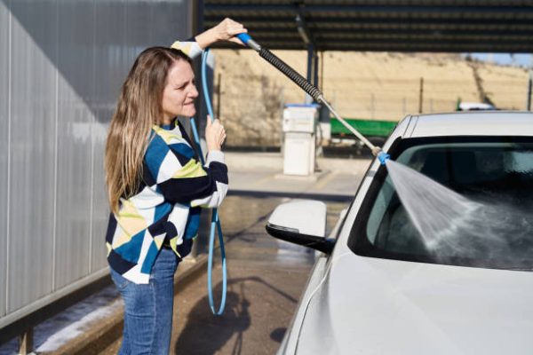 Profile view of caucasian blonde woman washing car at self-serve car wash with high pressure washer. Horizontal photography